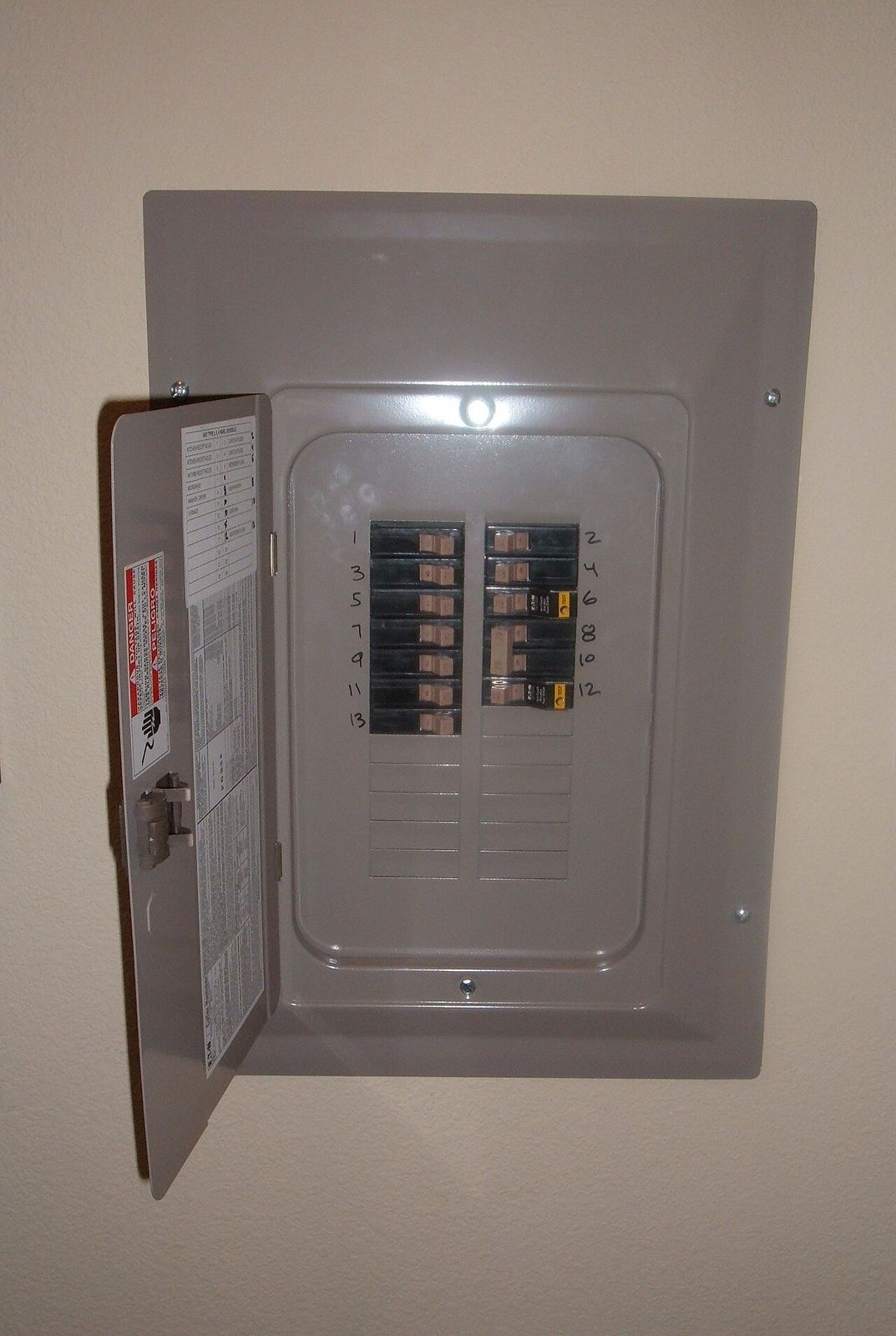 Open residential panel, cover off, breaker positions numbered in marker.